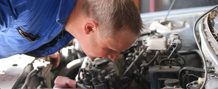 Ein Kfz-Mechaniker schaut prüfend in einen Motorraum. 